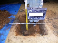 四角に地面が掘られ、目盛りで幅と深さを測り、黒板を持った職員がレーダー探査で確認された玉石を示した写真