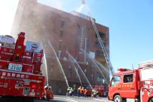 出初式で建物に消防車が一斉放水をしている写真