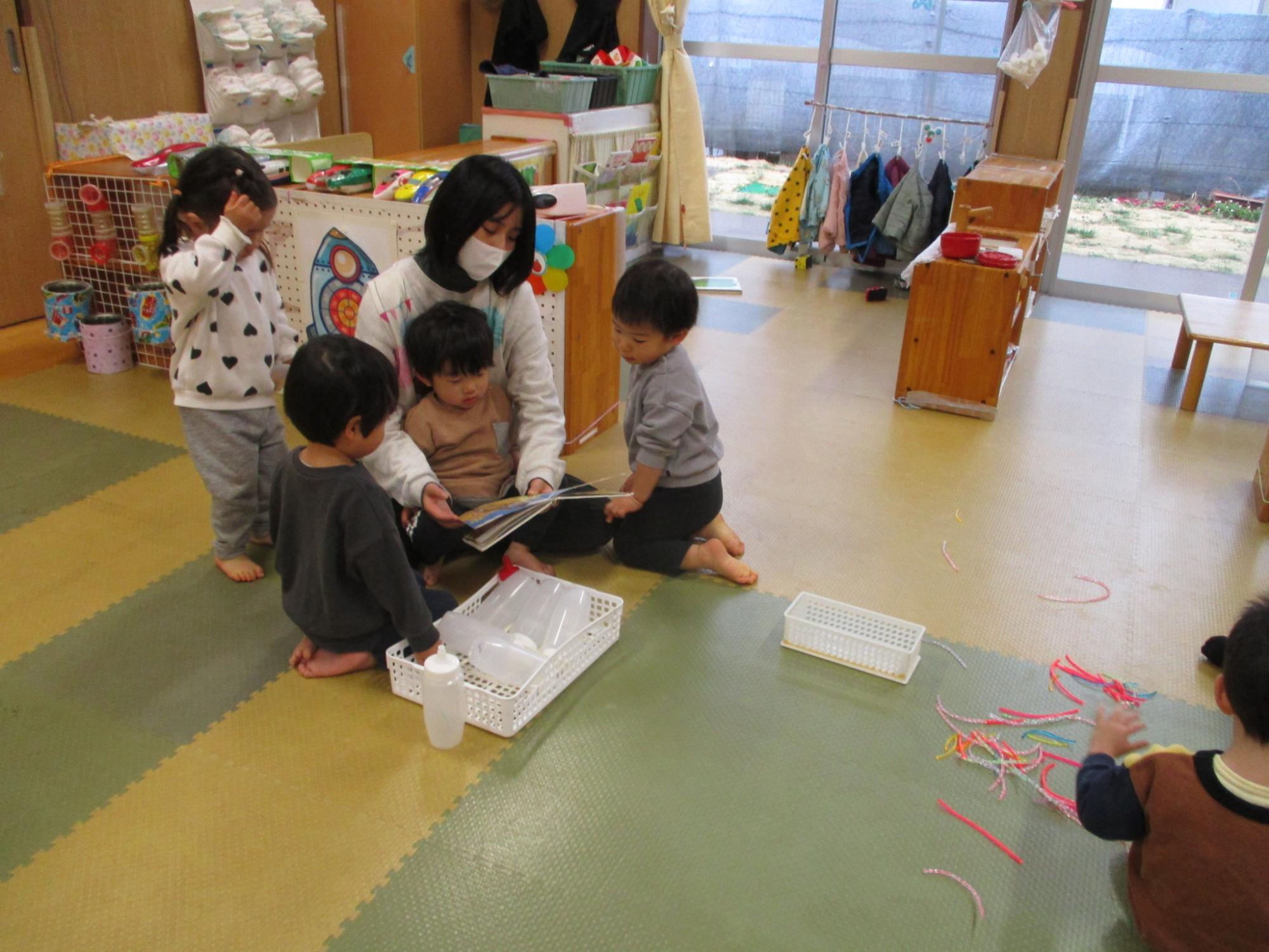 1歳児のこどもたちが保育士に絵本を読んでもらっています