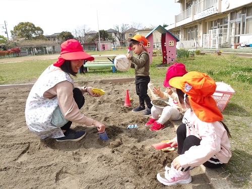 3歳児が砂場で保育者と一緒に遊ぶことを楽しむ様子