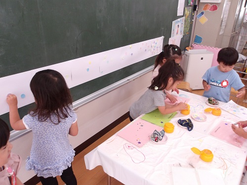 長い紙の台紙に画用紙を貼ることを楽しむ3歳児