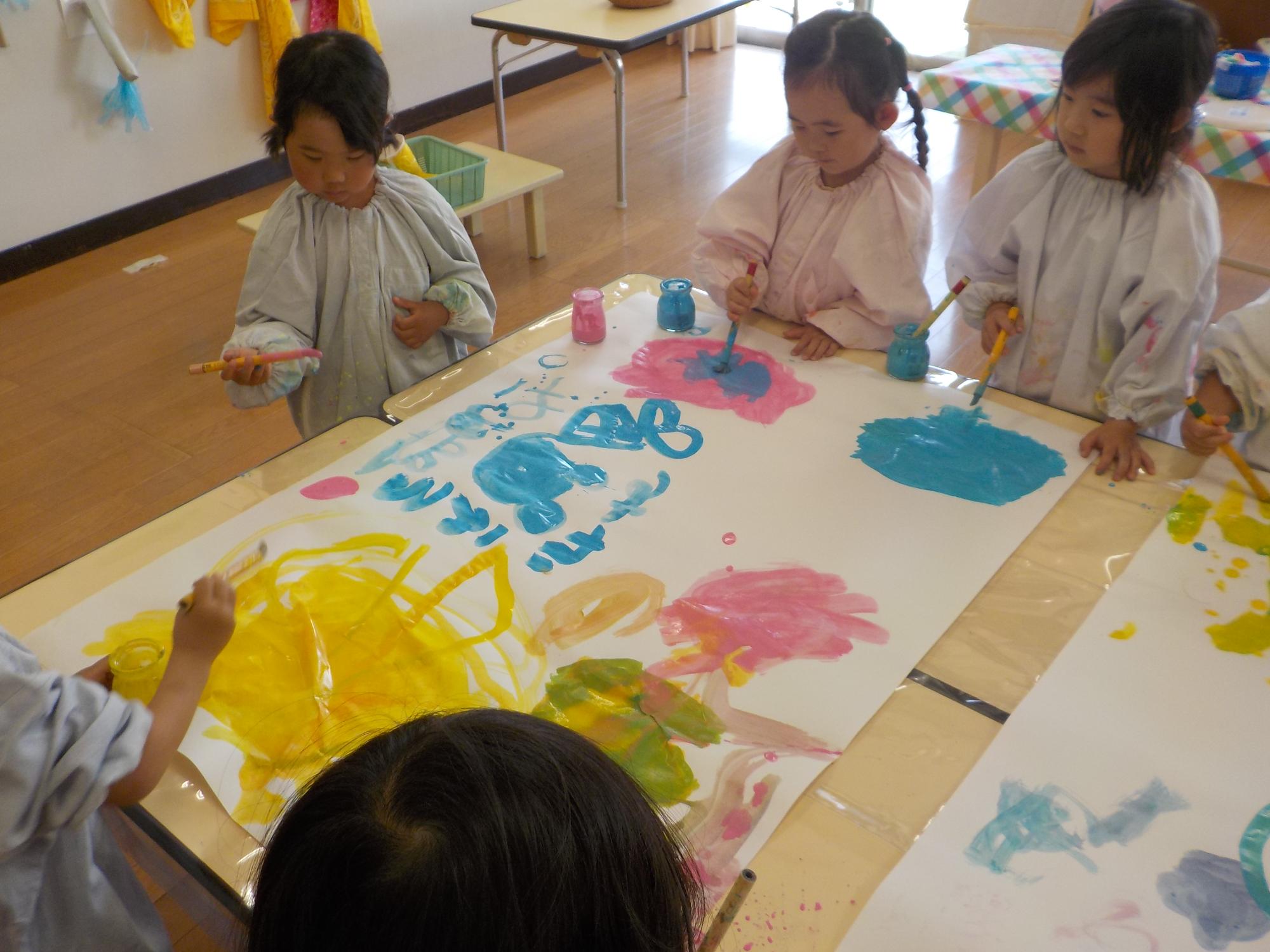 4歳児が大きな紙に絵の具で描いている