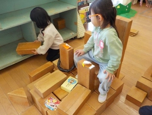 4歳児が箱積木で家や乗り物を作り、入ったり乗ったりして遊んでいる様子