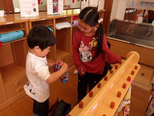 5歳児が3歳児にタオルのかけ方を教えている