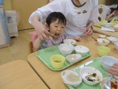 1歳児が保育者に手を添えてもらいながらご飯を食べているところ