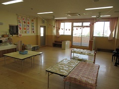 机やピアノが置かれ、天井に飾り付けがされている幼児組の保育室の写真