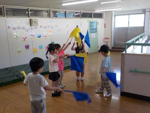 5歳児が黄色と青色の旗を持ってダンスをしています。