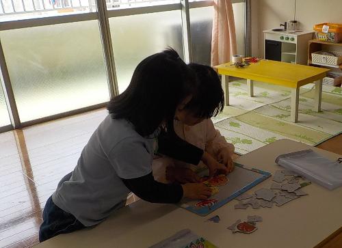5歳児が4歳児にパズルを教えてあげています