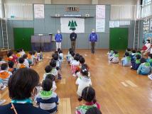 鹿野山少年自然の家の室内で、鹿野山の先生たちの話を体育座りして聞いている子供たちを後ろから写した写真