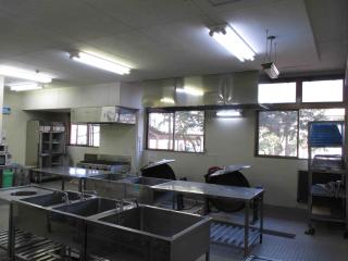 中央に2つの流し付きの作業台、手前に流しが設置されている体育館1階厨房設備の写真